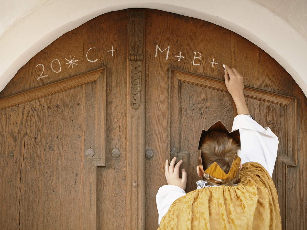 Ein Sternsinger schreibt den Segen "C+M+B" an eine Haustüre. (Foto: Benne Ochs/Kindermissionswerk)