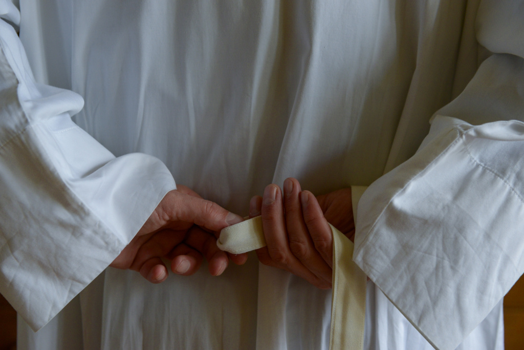 Ein Priester zieht in der Sakristei sein Messgewand an. Mit den Händen bindet der Priester die Kordel um den Körper. (Foto: KNA)
